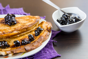 Pancakes with blueberries and blueberry jam on a plate and wooden table.