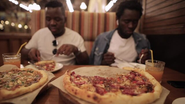 African Men Friends Eating Pizza In Restaurant