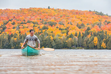 Man canoeing alone in a lake in Canada - Young man isolating and living the nature, autumn settings with colorful trees on background - Loneliness and isolation concepts
