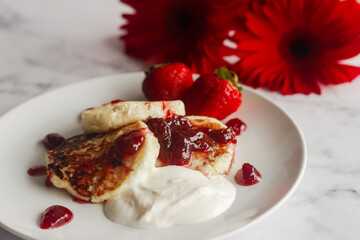 Tasty cheese pancakes with strawberries, sour cream and lingonberry jam. Cheese pancakes on a plate