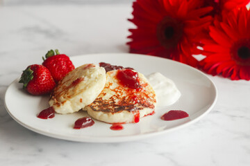 Tasty cheese pancakes with strawberries, sour cream and lingonberry jam. Cheese pancakes on a plate