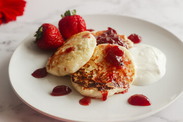Tasty cheese pancakes with strawberries, sour cream and lingonberry jam. Cheese pancakes on a plate