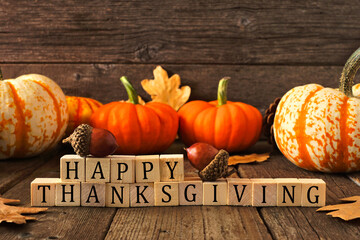 Happy Thanksgiving greeting on wooden blocks against a rustic wood background with pumpkins and...