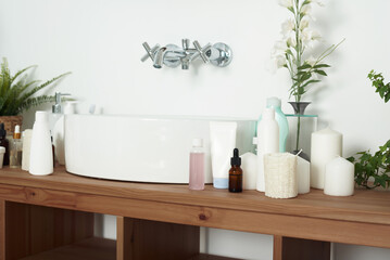 Light-colored bathroom sink with tubes of cream, jars of facial serums and clean towels. The concept of skin care, daily washing and cleanliness
