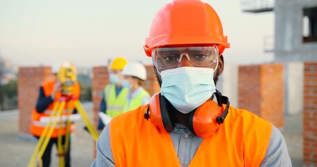 Portrait of African American man builder or construction manager in medical mask and protective...
