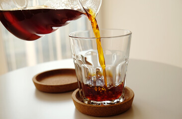 Black filter coffee pours from a jug into a glass close up. Specialty third wave concept