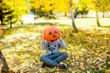 Child boy covering face with handmade pumpkin over autumn background. Halloween celebration concept