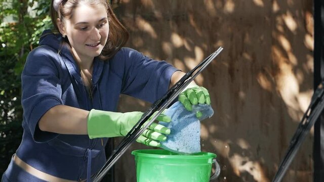 Young woman squeezes a blue sponge in a green bucket of water for washing a car, an image with car care content on a summer sunny day