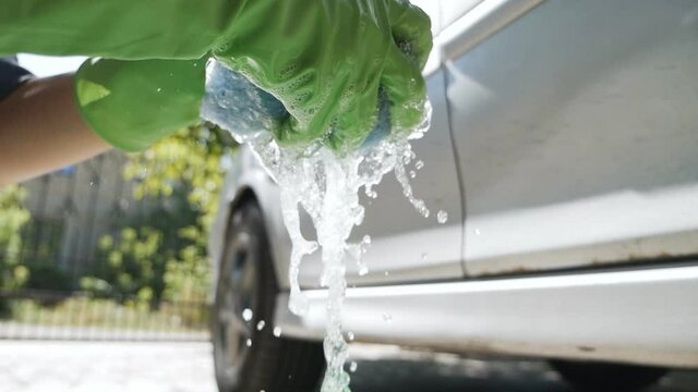 Hand squeezes a blue sponge in a green Bucket of water for a car wash, Image with car care content on a summer sunny day