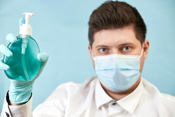 man in medical protective mask with antibacterial antiseptic gel for hand disinfection on blue background