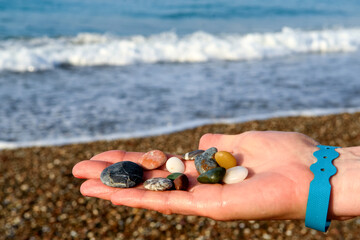 close-up of female hands holding colorful beach rocks with blurred beach background.
