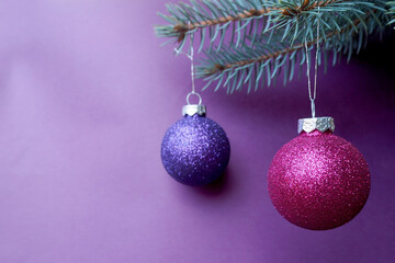 Obraz premium two round shiny purple and lilac Christmas balls are hanging on the Christmas tree on a lilac background . Christmas and new year symbols