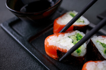 Chopsticks taking salmon maki roll from plate