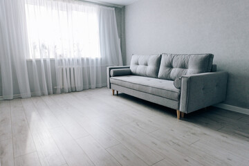Modern grey sofa with wooden legs in the room