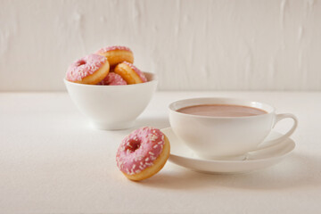 Mug of hot cocoa and donuts on white background. Tasty pink donuts and hot cacao cup. Sweet breakfast