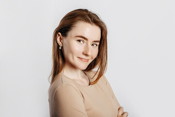 Beautiful young girl smiling and posing looking at the camera on a white isolated background. Positive brunette woman in a beige jumper. Kind look.