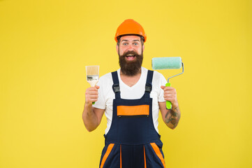 Happy painter in working clothes hold paint roller and brush painting tools for building and construction work, finishing - obrazy, fototapety, plakaty