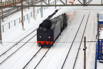 retro steam locomotive with one burning headlight rides on the railroad in winter