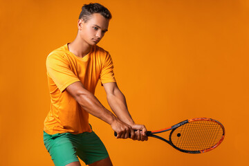 Fototapeta premium Studio shot of a young tennis player holding racket against orange background