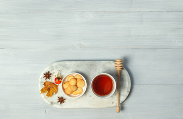 Autumn concept. A Cup of tea with honey and a bowl of cookies on a marble stand. On a grey wooden background with space, top view