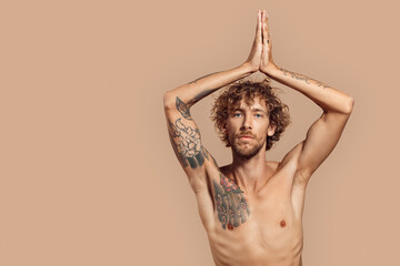 Freestyle. Man with curly hair and bare upper body standing isolated on beige hands in prayer above...