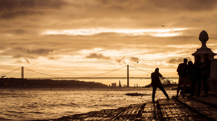 silhouette of tourist taking a picture of the famous 25th April suspension bridge on sunset background
