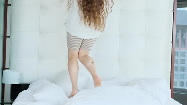 young woman cheerfully jumping in bed at home or hotel, concept of beauty and health, vacation, good mood, female happiness
