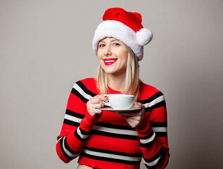 Smiling girl in Christmas hat with cup of coffee on grey background