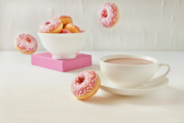 Flying pink donuts with a cup of cacao on a white background. selective focus on pink flying donuts