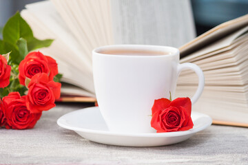 An open book with red orange roses and a cup of tea. Reading and relaxing. Romantic, sweet, dating concept.