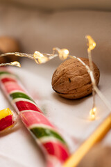 The atmosphere of Christmas and New Year. Colored candy canes, walnuts and garlands on a white background. Close-up