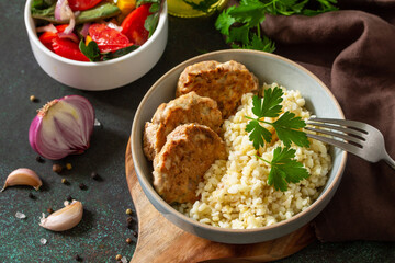 Healthy vegan food. Red fish cutlets with bulgur and fresh vegetable salad on a dark stone or slate table.