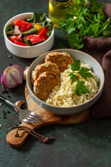 Healthy vegan food. Red fish cutlets with bulgur and fresh vegetable salad on a dark stone or slate table. Copy space.