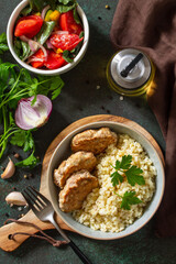 Healthy vegan food. Red fish cutlets with bulgur and fresh vegetable salad on a dark stone or slate table. Flat top view.