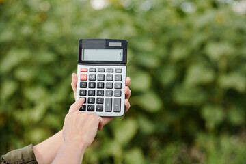 Hands of farmer holding calculator with one on its display and pushing button