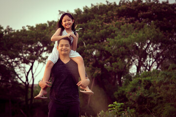 Fototapeta premium Asian little child girl riding on father's shoulders in the green natural background.Vintage color style