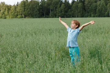 Naklejka na ściany i meble Caucasian boy on the field with a oats stands with his arms outstretched. Happy child