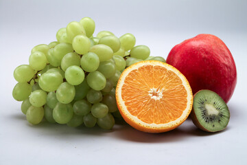 Close up to the fruits composition with green grapes, red apple, kiwi and orange on grey background. 