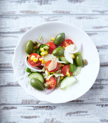 Healthy Salad with Green Olives, Baby Spinach, Cucumber, Cherry Tomatoes and Capers. Bright wooden background. Top view. Close up.	