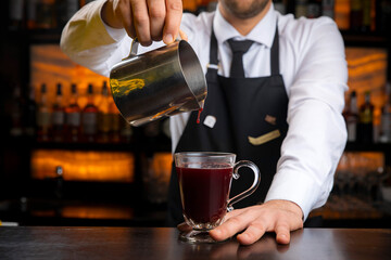 A young smiling bartender in a black apron prepares mulled wine
