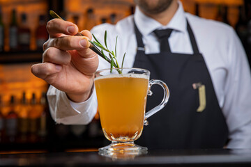 A young smiling bartender in a black apron prepares mulled wine
