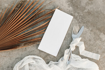 Tropical wedding ry still life. Closeup of blank menu card mock-up. Dry palm leaf, silver cutlery...