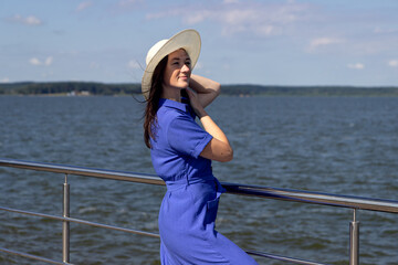 Young woman in hat on pier in stylish elegant dress poses enjoying amazing view.