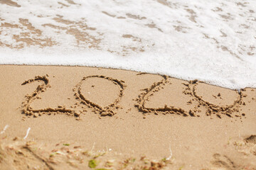 Good bye 2020 ! Wave with foam covering 2020 sign on sandy beach, leaving awful year 2020