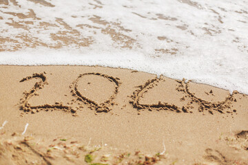 Good bye 2020 ! Wave with foam covering 2020 sign on sandy beach, leaving awful year 2020