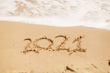 Hello 2021! Happy new year 2021 sign handwritten on sandy beach with waves and white foam