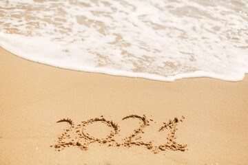 2021 handwritten sign on sandy beach with waves and white foam. Happy New year 2021