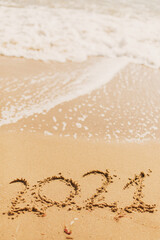 2021 handwritten sign on sandy beach with waves and white foam. Happy New year 2021
