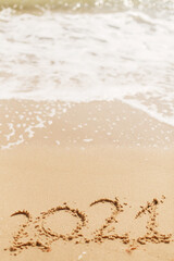 Hello 2021! Happy new year 2021 sign handwritten on sandy beach with waves and white foam