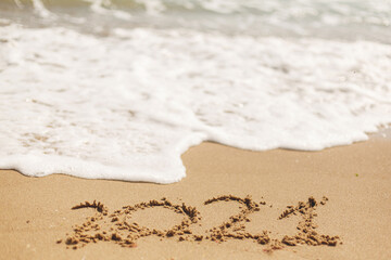Hello 2021! Happy new year 2021 sign handwritten on sandy beach with waves and white foam